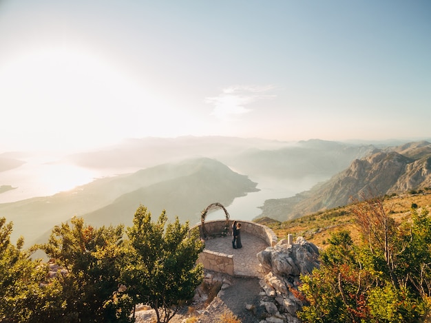 Gli sposi si abbracciano vicino all'arco nuziale sul ponte di osservazione sul Monte Lovcen che si affaccia sulla Baia di Kotor