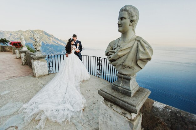 Gli sposi si baciano in piedi sul balcone sul mare