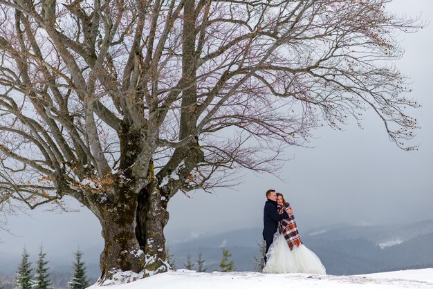 Gli sposi si coccolano sotto un tappeto per scaldarsi. Matrimonio invernale