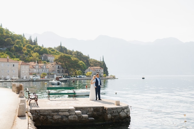 Gli sposi sono in piedi schiena contro schiena sul molo nella baia di Kotor