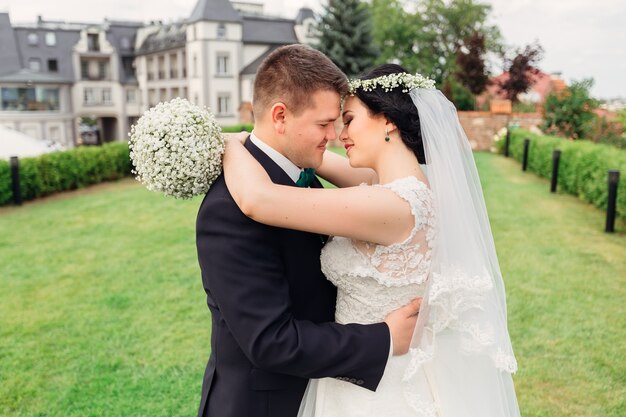 Gli sposini si abbracciano e vogliono baciare la sposa che tiene il bouquet da sposa nel cortile