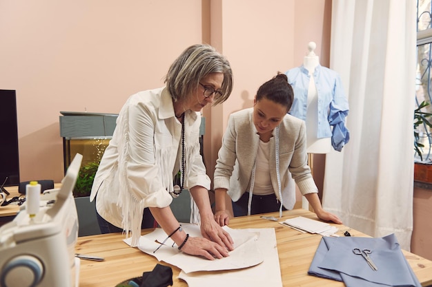 Gli stilisti creano nuovi stili alla moda discutono dei modelli durante lo sviluppo di una nuova collezione di abiti fatti a mano in un atelier di fashion design e sartoria