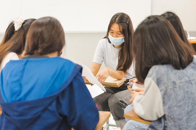 Gli studenti universitari asiatici del gruppo indossano una maschera protettiva per discutere il progetto in classe