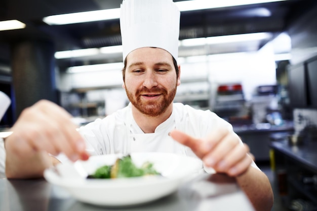 Gli ultimi ritocchi Inquadratura di uno chef che mette gli ultimi ritocchi su un piatto in una cucina professionale