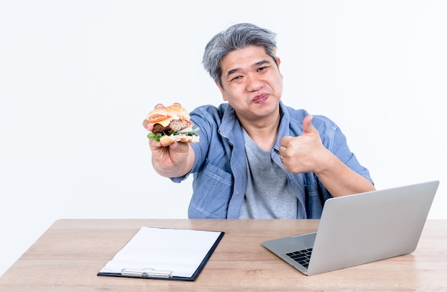 Gli uomini asiatici si divertono a mangiare hamburger mentre lavorava utilizzando un computer portatile