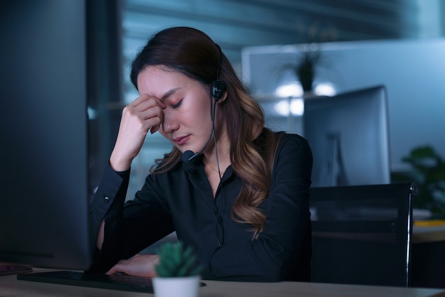 Gli uomini d'affari del call center delle donne asiatiche tailandesi hanno mal di testa ed emicrania dal lavoro a tarda notte