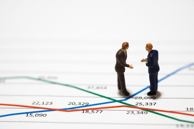 Gli uomini d&#39;affari di figure miniatura che stanno su un grafico del grafico di analisi esaminano la mano del documento la rassegna