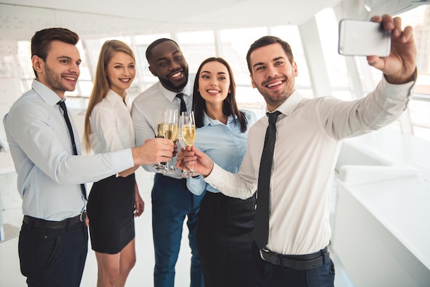 Gli uomini d'affari di successo bevono champagne parlando e sorridendo mentre festeggiano in ufficio Un ragazzo sta facendo selfie