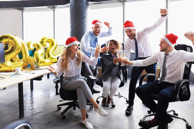 Gli uomini d'affari stanno festeggiando le vacanze in un ufficio moderno bevendo champagne e divertendosi nel coworking. Buon Natale e Felice Anno Nuovo 2022.