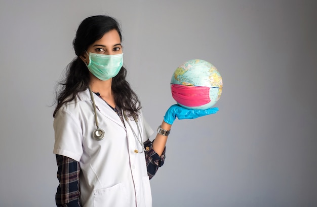 Globo del mondo della tenuta di medico della donna con una maschera di protezione della medicina. Epidemia mondiale del concetto di coronavirus.