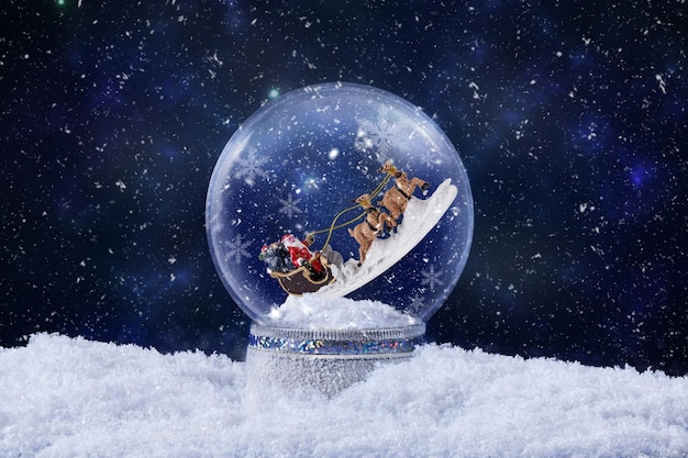 Globo di neve di Natale con Babbo Natale che cavalca le renne all'interno della carta di auguri di Natale con decorazione di sfera di neve magica con la neve che cade sullo sfondo di Natale