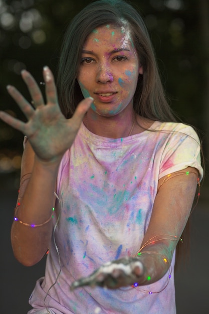 Gloriosa modella asiatica bruna che si diverte con la pittura Holi in posa con una ghirlanda sulle mani