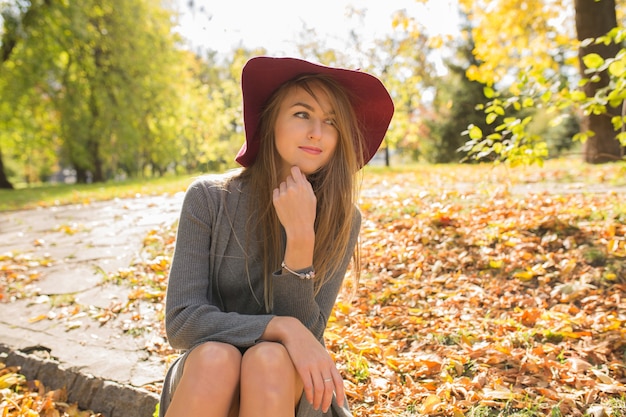 Gloriosa modella bionda con cappello rosso in posa nella foresta, indossando un abito in maglia alla moda