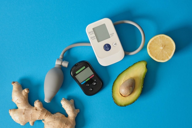 Glucometro monitor della pressione sanguigna zenzero limone e avocado su sfondo blu nutrizione per malattie cardiache