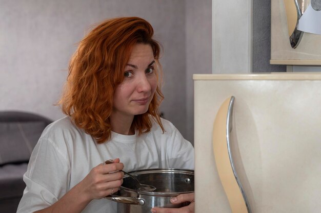 Glutton ragazza vicino al frigorifero mentre si mangia di notte Ragazza con una grande casseruola in mano