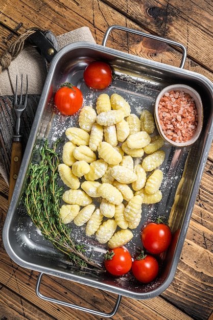 Gnocchi di patate crudi crudi nel vassoio d'acciaio della cucina con le erbe Fondo di legno Vista dall'alto