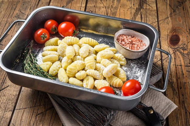 Gnocchi di patate crudi crudi nel vassoio d'acciaio della cucina con le erbe Fondo di legno Vista dall'alto