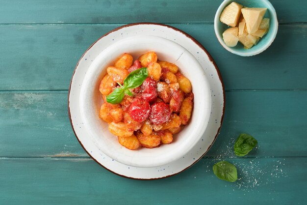 Gnocchi di patate gnocchi tradizionali di patate fatti in casa con salsa di pomodoro basilico e formaggio parmigiano su fondo di tavola di cucina rustico turchese cibo tradizionale italiano vista superiore