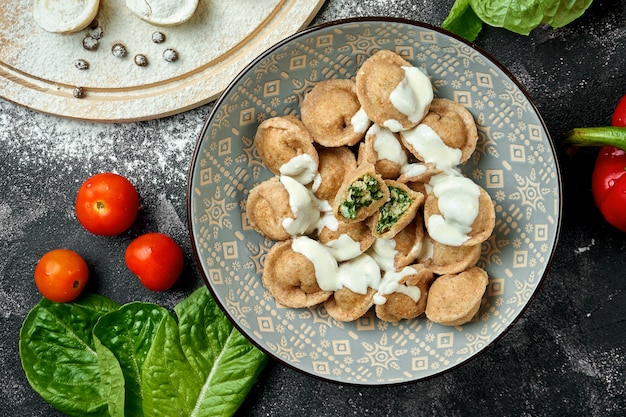 Gnocchi fatti in casa con spinaci e tacchino in una ciotola su un tavolo scuro. Gnocchi in una composizione con verdure e ingredienti. Vista dall'alto