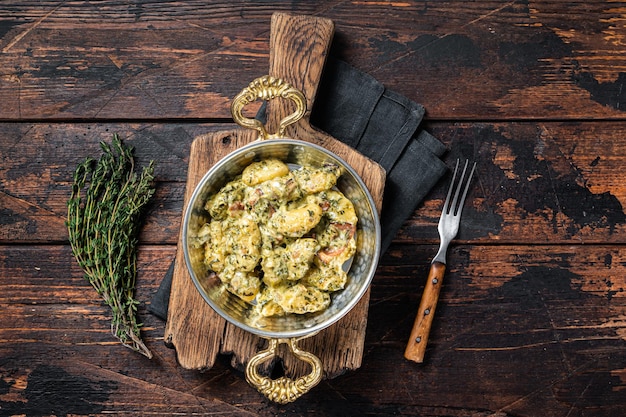 Gnocchi italiani di patate con spinaci e parmigiano in padella. Fondo in legno. Vista dall'alto.