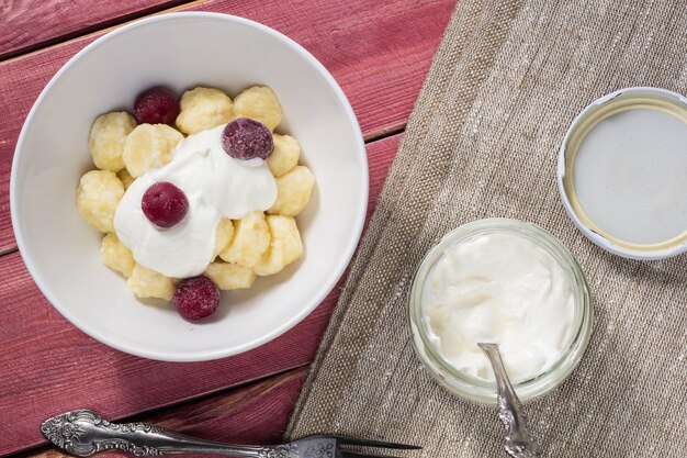 Gnocchi pigri di ricotta ucraina russa tradizionale serviti con panna acida e ciliegia su fondo di legno