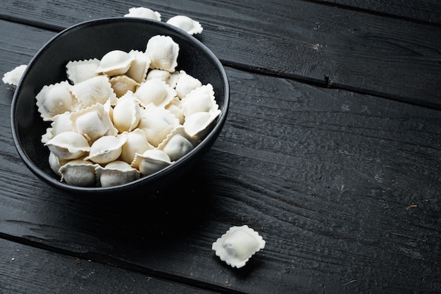 Gnocchi surgelati tortellini e ravioli messi in ciotola nera, su sfondo nero tavolo in legno, con copyspace e spazio per il testo