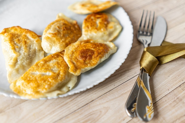 gnocchi varenyky arrostiti su un piatto bianco con un fiocco di seta intorno alle posate su fondo di legno wooden