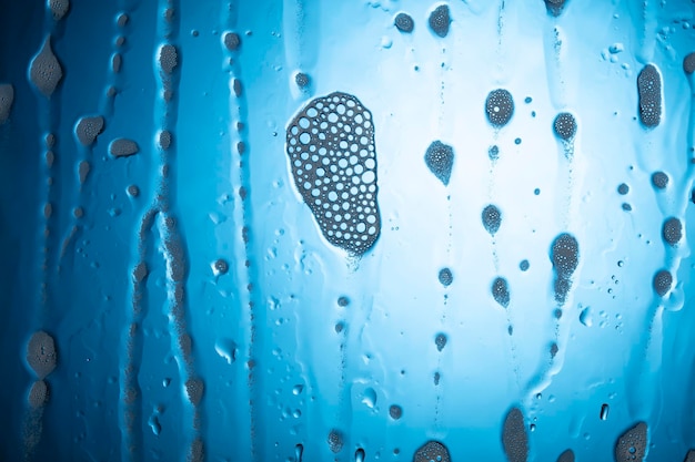 Gocce d'acqua con schiuma su vetro su sfondo blu.