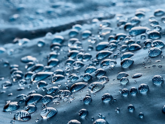 Gocce d'acqua piovana su tessuto impermeabile in fibra blu. Sfondo blu.