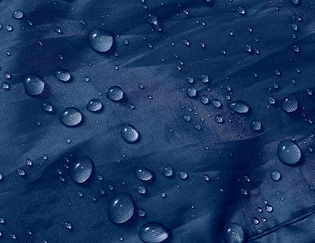 Gocce d'acqua su tessuto a membrana impermeabile. Vista in dettaglio della trama del panno impermeabile blu.