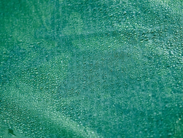 Gocce d'acqua su tessuto a membrana impermeabile. Vista in dettaglio della trama del panno impermeabile sintetico verde. Rugiada mattutina sulla tenda.