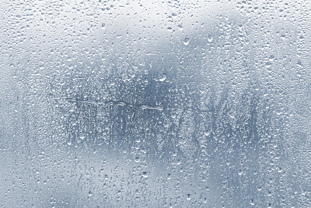 Gocce di pioggia, condensa sulla finestra di vetro durante la pioggia, gocce d'acqua su vetro blu