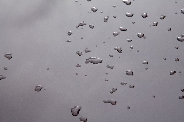 Gocce di pioggia e riflesso del cielo sul cofano di un'auto grigia. Gocce d'acqua dopo la pioggia su metallo verniciato