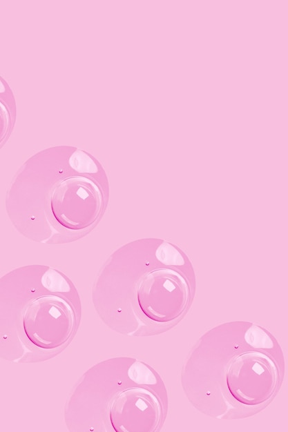 Gocce rotonde di siero gel trasparente su sfondo rosa gel con bolle Gocce d'acqua