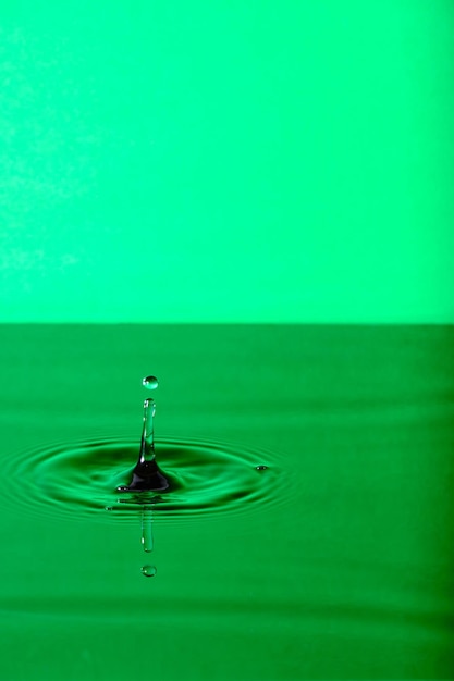 Goccia d'acqua spruzzata con cerchi d'acqua divergenti su sfondo verde
