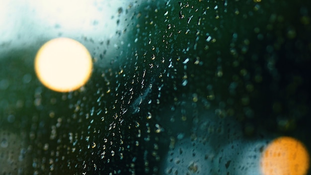 Goccia di pioggia sulla finestra di notte. Finestra del soggiorno di un appartamento o di un condominio sulla notte della stagione delle piogge a Bangkok in Thailandia. La finestra esterna è sfocata bokeh di pioggia di luce della città e albero naturale e cielo.