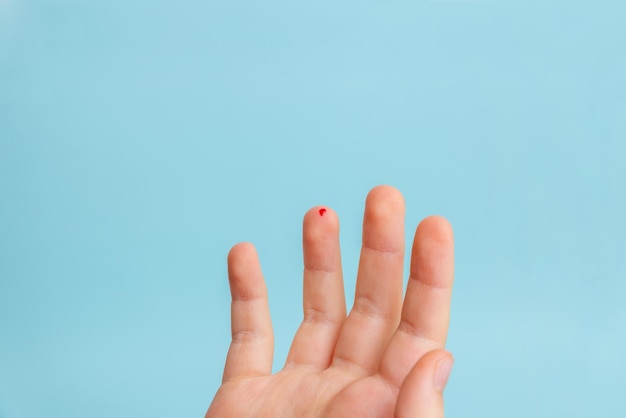 Goccia di sangue sul dito di un bambino. Il concetto di misurare i livelli di zucchero nel sangue con l'aiuto di strisce. Sfondo blu