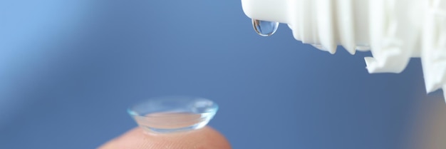 Goccia trasparente che gocciola dalla bottiglia sul primo piano della lente a contatto usando gocce per gli occhi asciutti quando