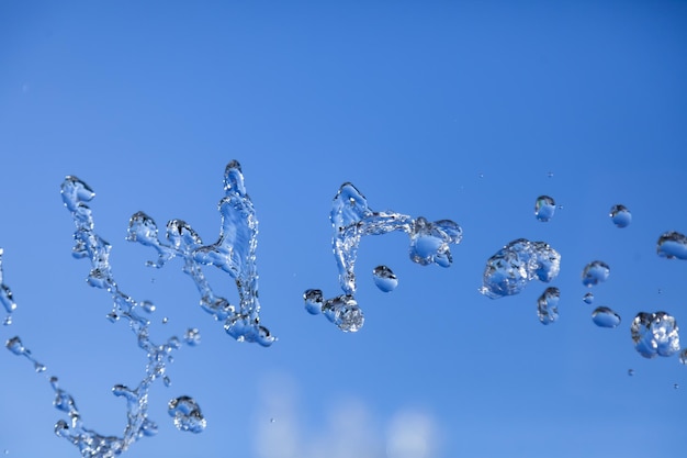 Goccioline d'acqua congelate nell'aria con spruzzi e bolle a catena su uno sfondo blu isolato in natura Liquido chiaro e trasparente che simboleggia la salute e la natura