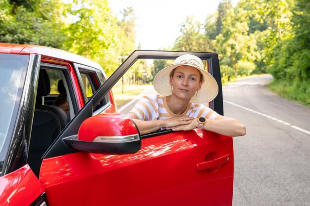 Godendo dell'acquisto in concessionaria affittare un concetto di viaggio in autopositiva ragazza allegra autista funky godere di successi musicaliAllegra giovane femmina è vicino a un'auto rossa lucida