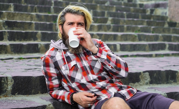 Godendo di caffè fresco uomo barbuto in abbigliamento casual con tazza di caffè da asporto buongiorno