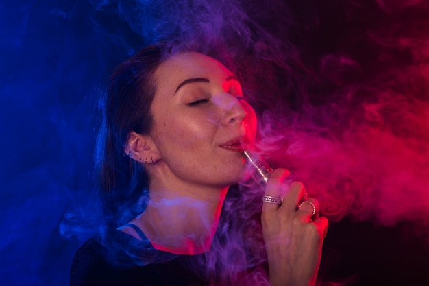 Godendo di donna con vape o sigaretta elettronica in fumo e luce al neon.