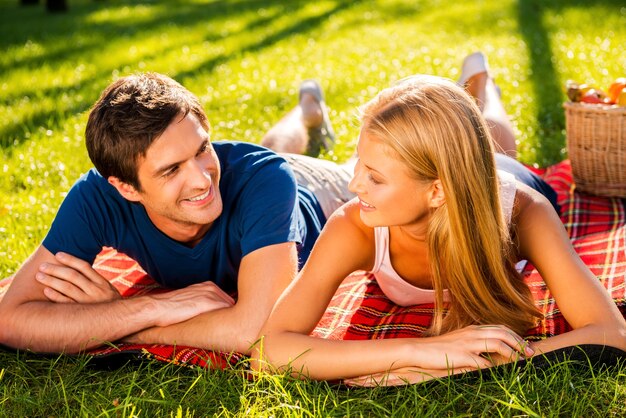 Godendo il loro appuntamento perfetto insieme. Felice giovane coppia di innamorati che si rilassano nel parco insieme mentre sono sdraiati su una coperta da picnic e si guardano l'un l'altro