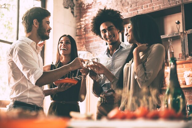 Godendo la festa con gli amici. Inquadratura dal basso di giovani allegri che applaudono con flauti di champagne e sembrano felici mentre fanno festa a casa