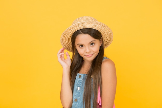 Godendo la vacanza. Buone vibrazioni. Stile da spiaggia. Piccola bellezza in cappello di paglia. Vestito elegante. Moda estiva per ragazze adolescenti. Vacanze estive. Ritratto di ragazza allegra felice in estate cappello sfondo giallo.