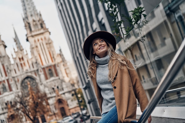 Godendo una bella giornata. Attraente giovane donna che guarda lontano e sorride mentre trascorre del tempo spensierato in città