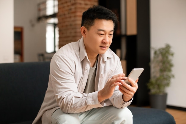 Godersi il tempo libero uomo asiatico di mezza età che utilizza lo smartphone navigando in Internet o inviando messaggi sui social