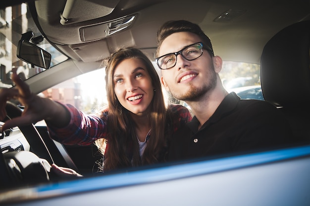 Godersi il viaggio. Bella giovane coppia seduta sui sedili del passeggero anteriore e sorridente mentre un bell'uomo alla guida di un'auto.