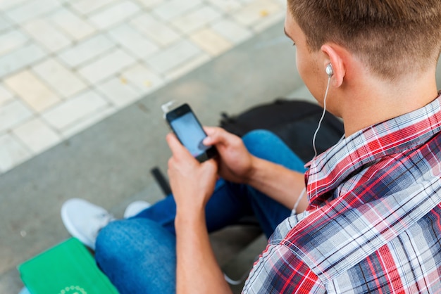 Godersi la musica all'aperto. Vista dall'alto del giovane che ascolta il lettore MP3 mentre è seduto sulla scala all'aperto