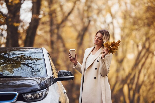 Godersi la natura. La ragazza ha un viaggio autunnale in auto. Automobile nuova di zecca moderna nella foresta.